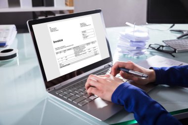 Close-up Of A Businessperson's Hand Analyzing Invoice On Laptop At Workplace clipart