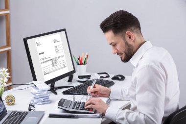 Genç işadamı masasında hesap makinesiyle fatura hesaplama