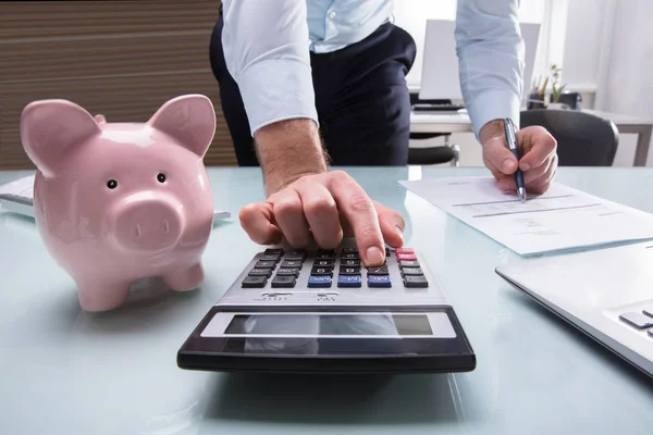 Geschäftsmann Mit Taschenrechner Zur Rechnungsberechnung Mit Sparschwein Auf Dem Schreibtisch — Stockfoto