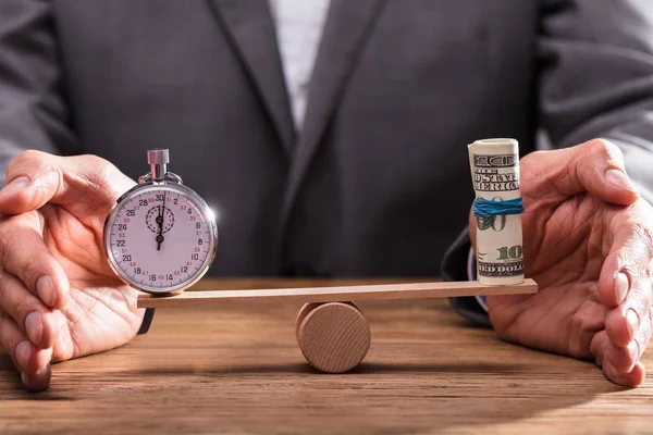 一个商人的手保护平衡秒表和卷起钞票在跷跷板上的特写 — 图库照片