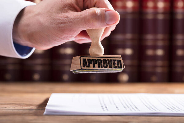Close-up Of A Judge's Hand Approving Contract Form In Courtroom