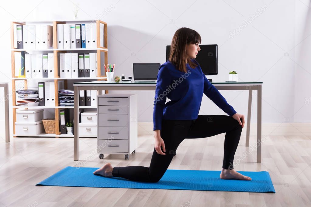 Side View Of A Young Businesswoman Doing Workout On Exercise Mat In Office