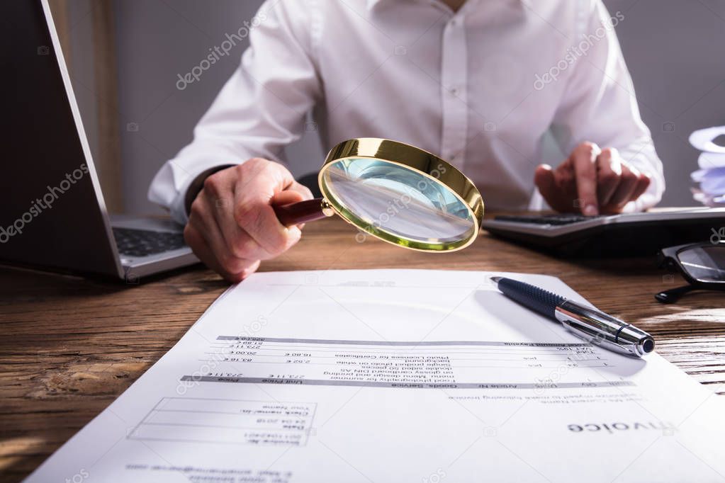Businessperson Analyzing Bill Through Magnifying Glass On Desk