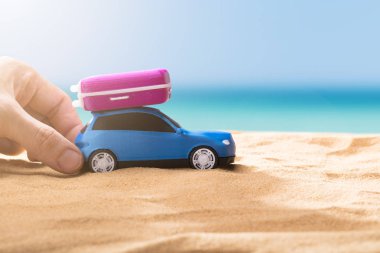 Bir kişinin el Bagaj ile mavi araba Sandy Beach üzerinde tutarak