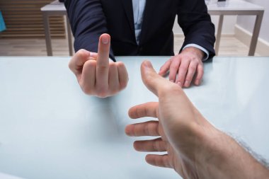 Close-up Of Businessman's Hand Showing Middle Finger To His Partner In Office clipart