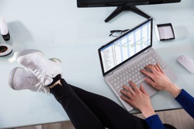 İşadamı'nın el ofis masasında çapraz ayaklı dizüstü kullanarak Gantt grafiği üzerinde çalışıyor