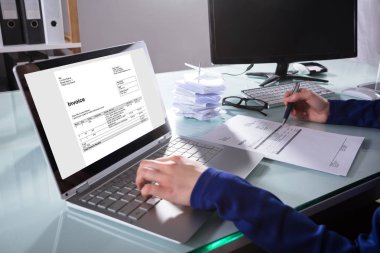 Close-up Of A Businessperson's Hand Checking Invoice On Laptop In Office clipart