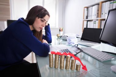 Red Arrow Over Decreasing Stacked Coins Showing Downward Direction In Front Of Upset Businesswoman clipart