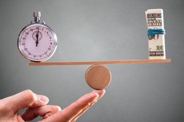 A Person Hand With Balance Between Stopwatch And Rolled Up Banknotes On Seesaw clipart