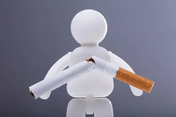 灰色の背景に壊れたタバコを持つ人間の姿 — ストック写真