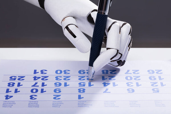 Close-up Of A Robotic Hand Marking Date On Calendar With Pen