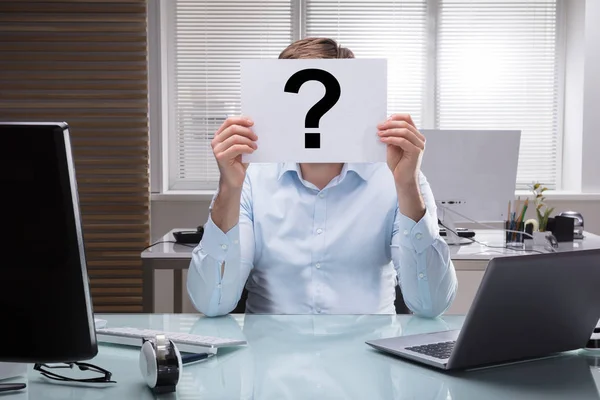 Businessperson Holding Placard With Question Mark Sign In Front Of Face In Office