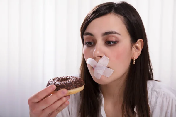 一个年轻女人的特写 她的嘴上粘胶带无法吃甜甜圈 — 图库照片