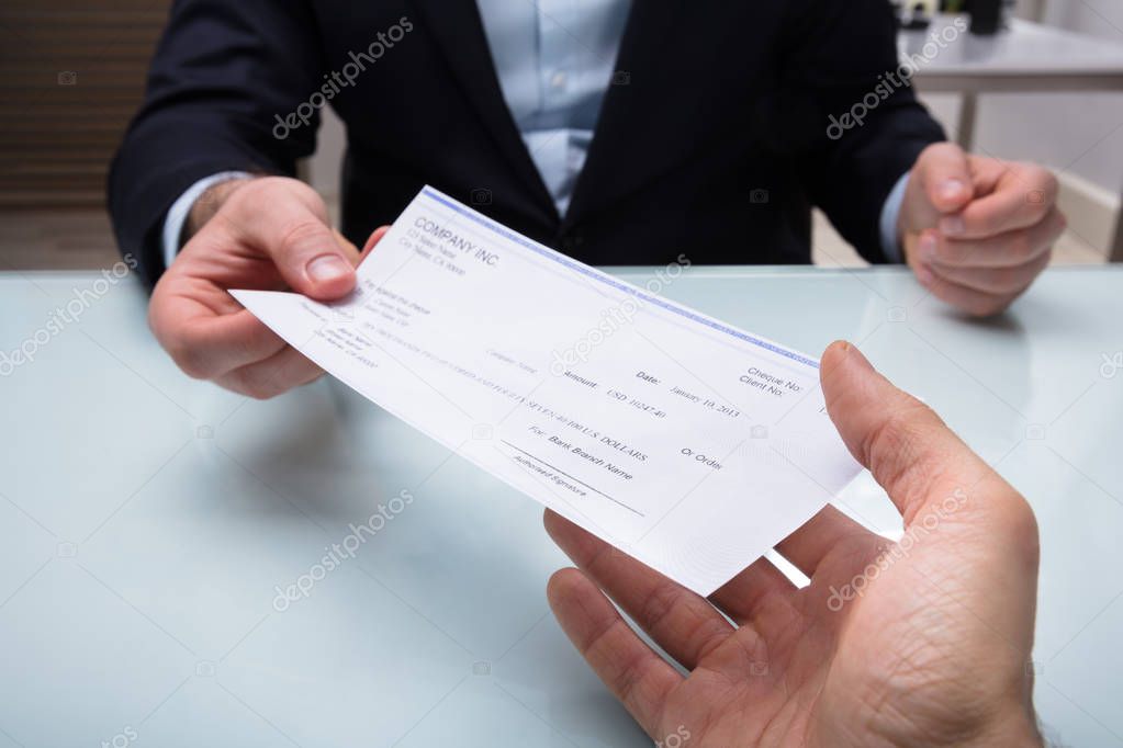 Close-up Of A Businessman's Hand Giving Cheque To His Colleague At Workplace