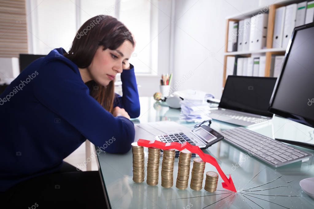 Red Arrow Over Decreasing Stacked Coins Showing Downward Direction In Front Of Upset Businesswoman