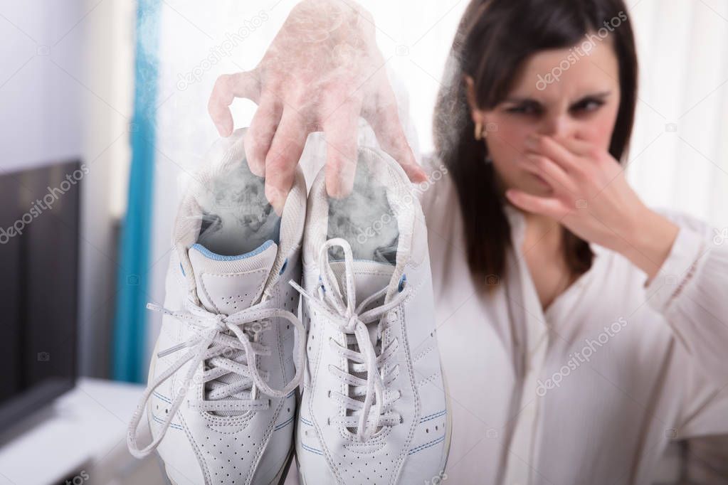 Woman Holding Her Smelling Exercise Shoe With Steam Coming Out From It