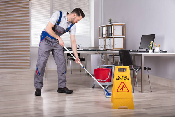 Man Cleaning Office With Mop Near Caution Wet Floor Sign
