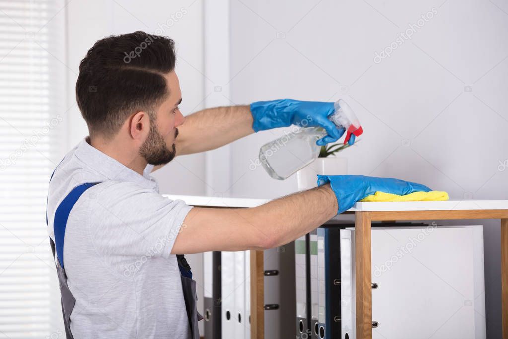 Close-up Of A Young Male Cleaner Cleaning Shelf At Workplace