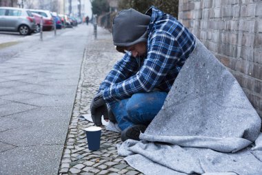 Side View Of A Male Beggar Sitting On Street Near Disposable Cup clipart