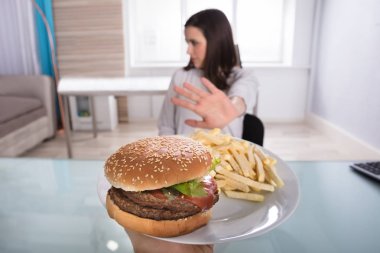 Genç kadın hamburger ve patates kızartması plaka üzerinde reddediyor