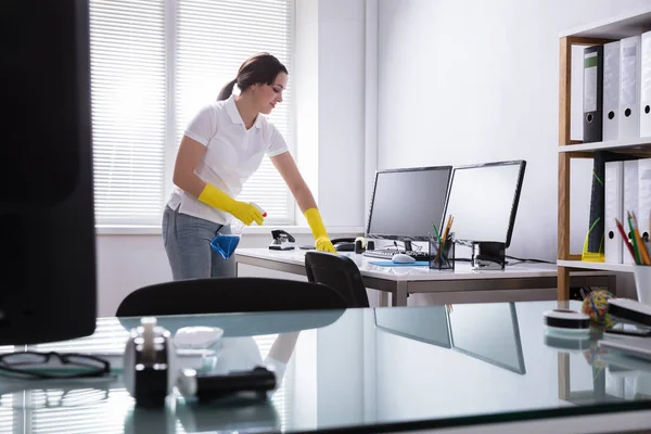 年轻妇女清洁计算机与抹布在办公室里 — 图库照片