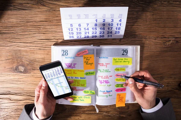 在日记中使用手机写日程表的生意人的高角度看法 — 图库照片