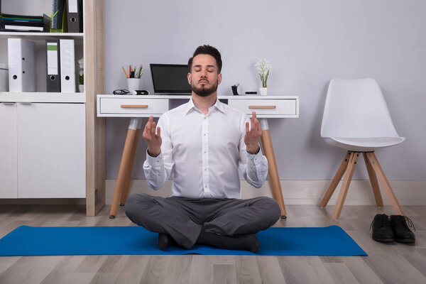 Спокойный молодой бизнесмен, сидящий на упражнениях мат медитируя в офисе
