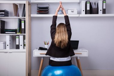 Kollarını germe Fitness topu üzerinde oturan bir iş kadını arkadan görünüş