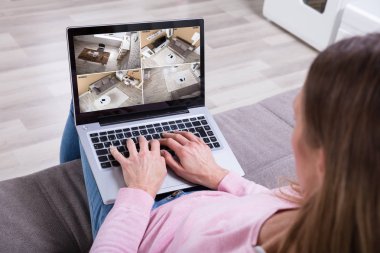 Close-up Of Woman Sitting On Couch Monitoring Home Security Cameras On Laptop At Home clipart