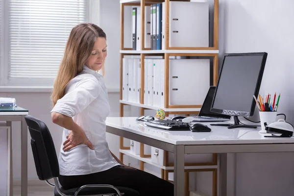 一个成熟的女商人坐在椅背疼痛的侧面视图 — 图库照片