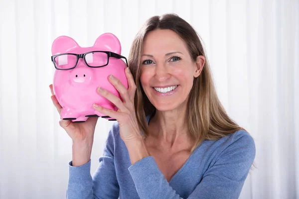 Smiling Mature Woman Holding Pink Piggybank Black Eyeglasses White Blinds — Stock Photo, Image