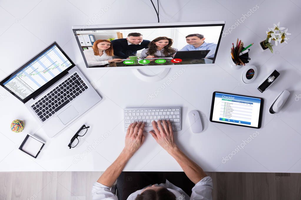 Businessperson Video Conferencing On Computer With Laptop And Digital Tablet On Desk