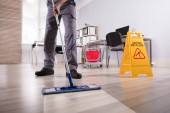 Unterer Abschnitt der männlichen Hausmeister Reinigung Boden mit Vorsicht nassen Fußboden Schild im Büro