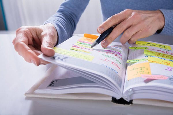 Close-up Of A Woman Writing Schedule In Calendar Diary On White Desk