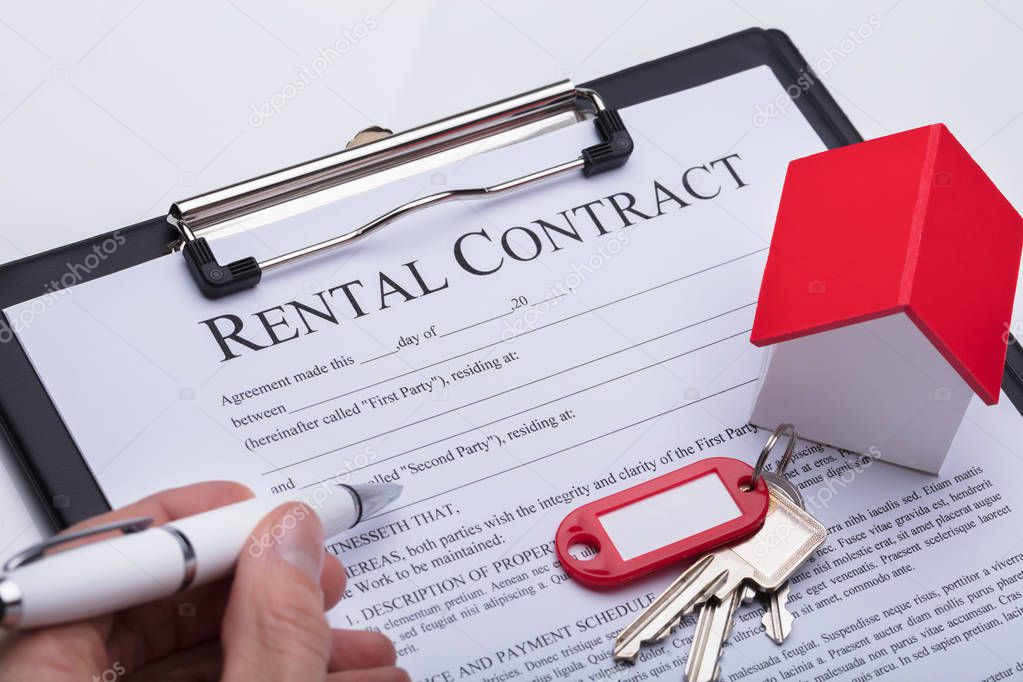 Close-up Of Key Over A Person's Hand Filling Rental Contract Form