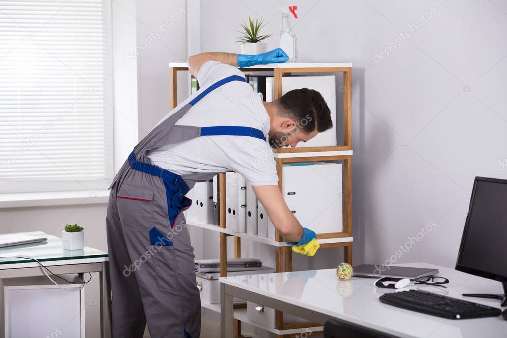 Close-up Of A Young Male Cleaner Cleaning Shelf At Workplace