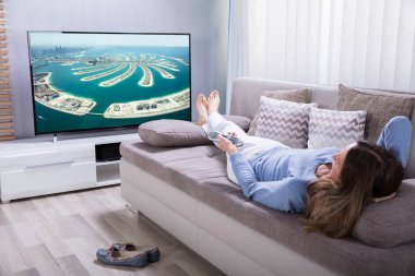 Evde Jumeirah Palmiye Adası geliştirme televizyon izlerken kanepede yatan kadın