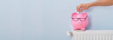 Piggybank 'e evdeki radyatörün üzerinden para sokan kişi.