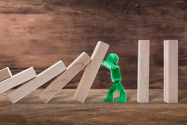 Side View Of A Green Plastic Figure Stopping The Wooden Domino Effect On Plank