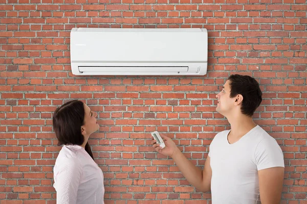 Pareja Joven Encendiendo Aire Acondicionado Con Control Remoto Pared Ladrillo — Foto de Stock