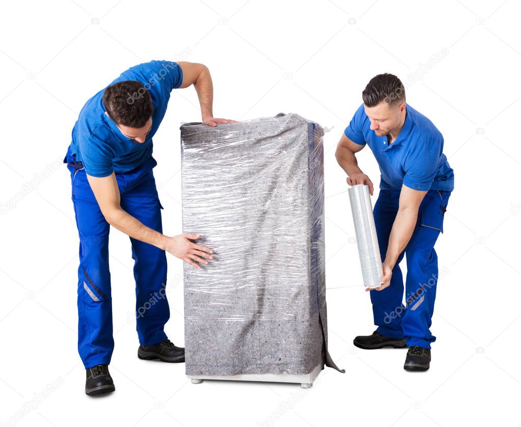 Two Male Movers Wrapping The Home Appliances With Plastic Wrap On White Background