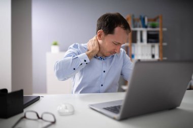 Young Man Suffering From Neck Pain While Working On Laptop clipart