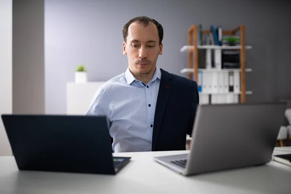 Businessperson Doing Multitasking Work On Two Laptops At Workplace