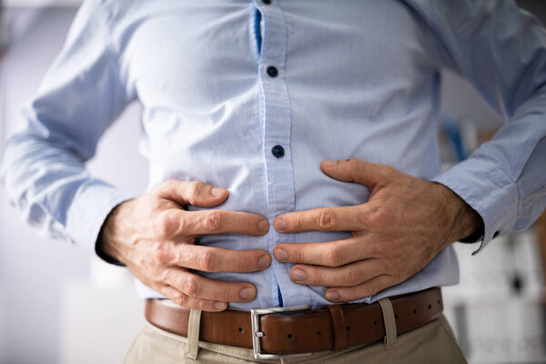 Средняя часть бизнесмена, страдающего от болей в животе на белом фоне
