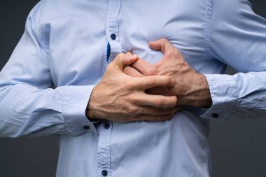 Midsection Of A Man Wearing Blue Shirt Suffering From Heart Attack Standing Against Grey Background clipart