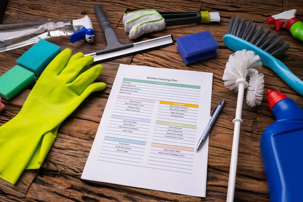 Close-up Of Various Cleaning Products Around Weekly Cleaning Plan Form With Pen