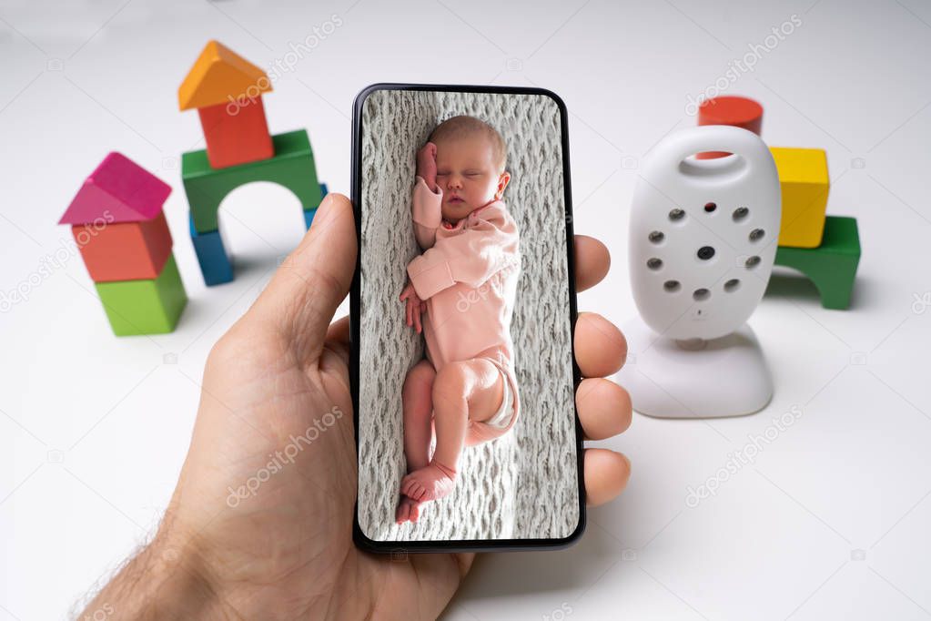 Person's Hand Holding Mobile Phone With Baby Image Near Wireless Camera