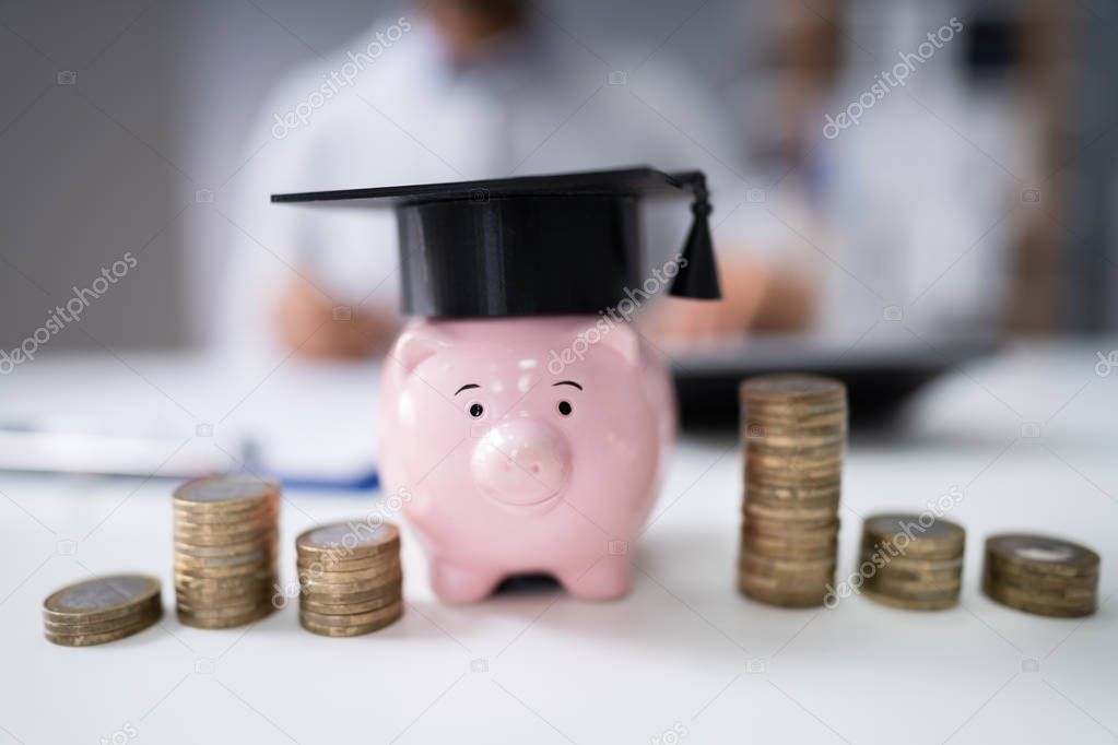 Stacked Coins And Piggy Bank With Graduation Cap In Front Of Businessman
