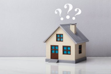 Gri Arkaplan Karşısında Yansıtıcı Masa Üzerinde Soru İşaretleri Olan Küçük Ev Modeli