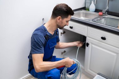 Male Plumber Cleaning Clogged Sink Pipe In Kitchen clipart